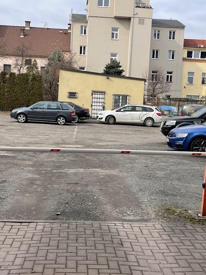 Pohled přes parkoviště na žlutý domeček